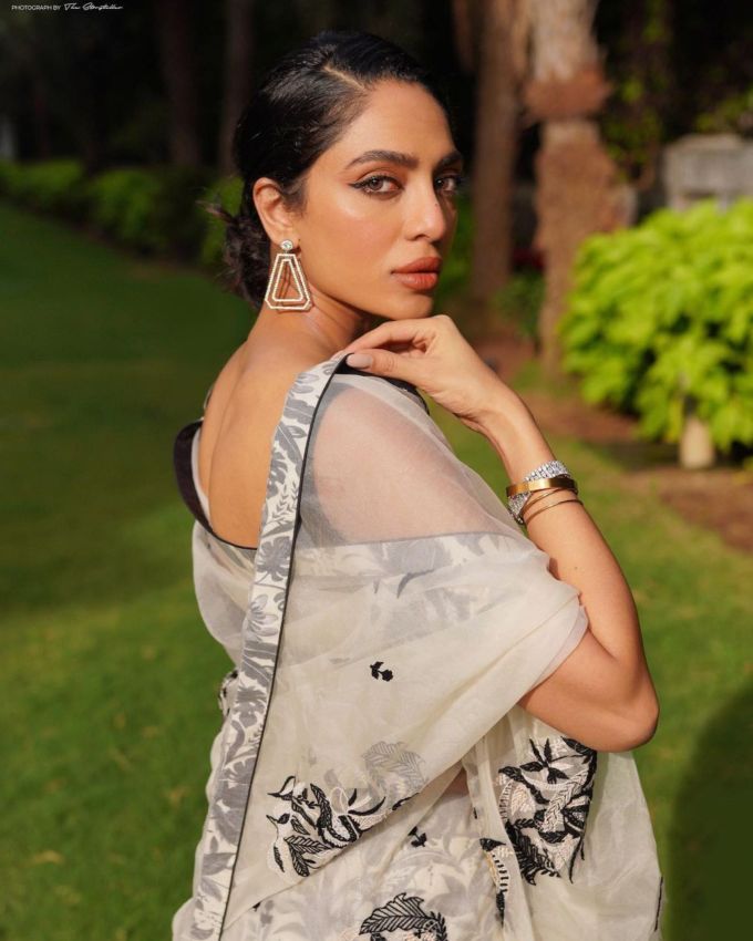 શોભિતા ધૂલિપાલા વાઈટ નેટ સાડી : શોભિતા ધૂલિપાલાએ વાઈટ કલર નેટ સાડી પસંદ કરી છે જેમાં બ્લેક ફ્લોરલ ડિઝાઇન અને બ્લેક બોર્ડર જોવા મળે છે, આ સાડી ટ્રાંસપેરન્ટ છે અને એમાં બ્લેક ડીપ વી શેપ નેકલાઇન વાળો સ્લીવલેસ બ્લાઉઝ પસંદ કર્યો છે.