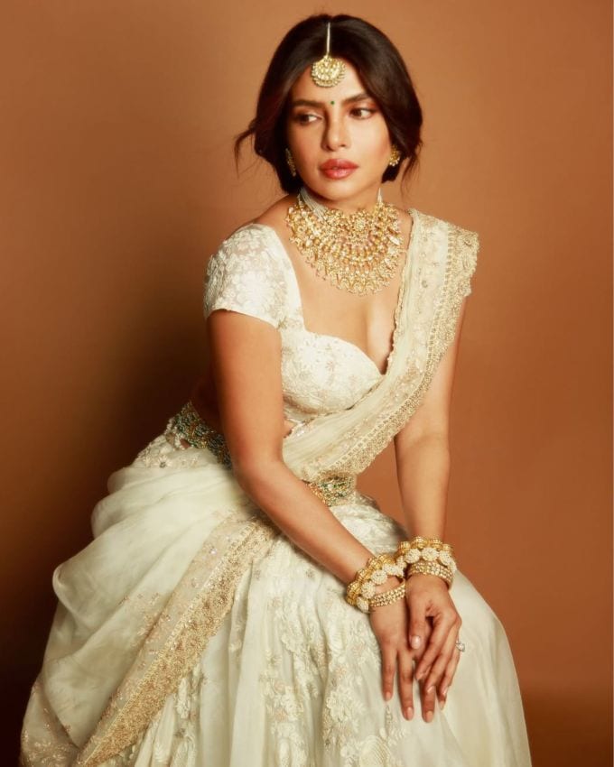 <strong>પ્રિયંકા ચોપરા મંદાકિની લુક </strong>: અમી પટેલ દ્વારા સ્ટાઇલ કરાયેલ ચોપરાએ તેના લેસ એમ્બ્રોઇડરીવાળા લહેંગાને ગોલ્ડન બ્રોકેડ વર્ક સાથે ગોલ્ડન બંગડીઓ, એક ડિટેઇલ નેકપીસ અને મેચિંગ માંગ ટીકા અને કાનની બુટ્ટીઓ સાથે જોડી દીધી હતી. ગોલ્ડ અર્ધચંદ્રાકાર શેપના એક્સેસરીઝથી શણગારેલી ઢીલી ફિશટેલ વેણીએ તેના આઉટફિટમાં શાહી ગ્લેમનો ટચ ઉમેર્યો હતો. સોફ્ટ ડિયુ મેકઅપ, ઘણા બધા બ્લશ અને ન્યૂડ ગ્લોસી લિપ્સ, અને કમરની ચેઇનને પૂરક બનાવે છે, જે આખા લુકને અદભુત બનાવે છે.